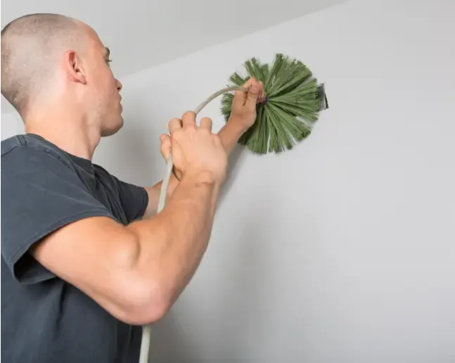 Technician cleaning an air duct with a rotary brush tool.