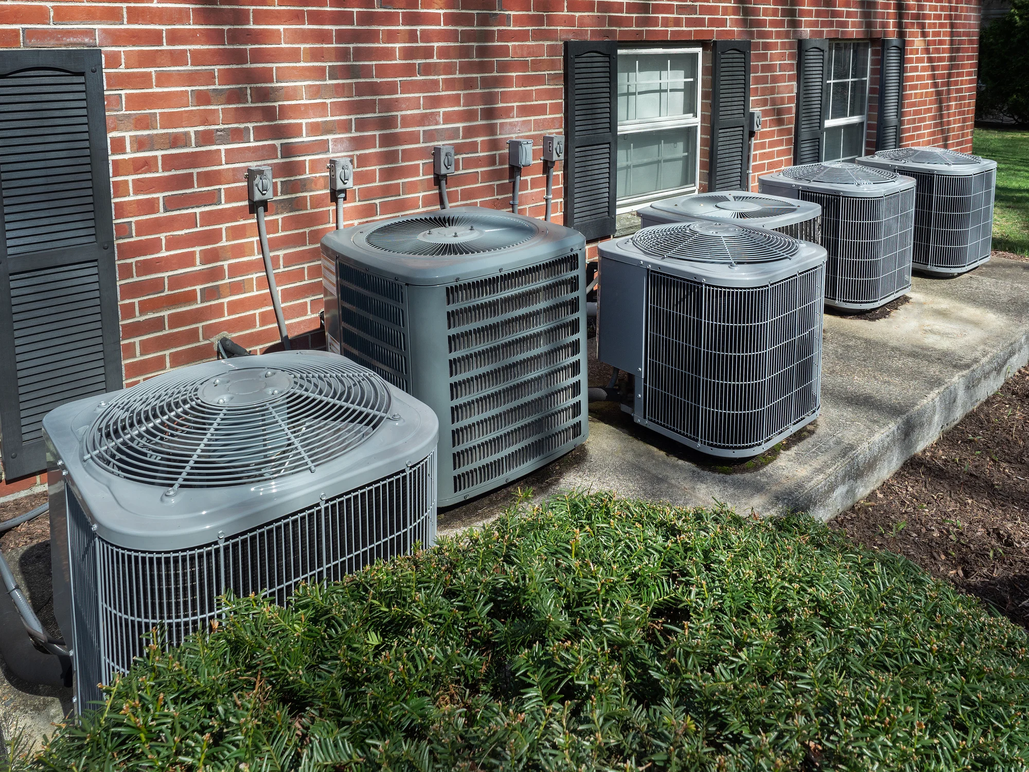 Multiple residential HVAC units outside a multi-family brick building.