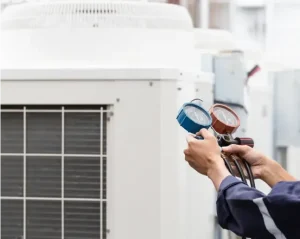 Technician using HVAC gauges to check refrigerant levels on an outdoor commercial unit.
