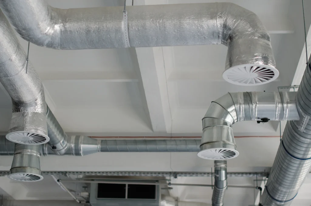Exposed commercial HVAC ductwork system with metal air vents installed on a ceiling.