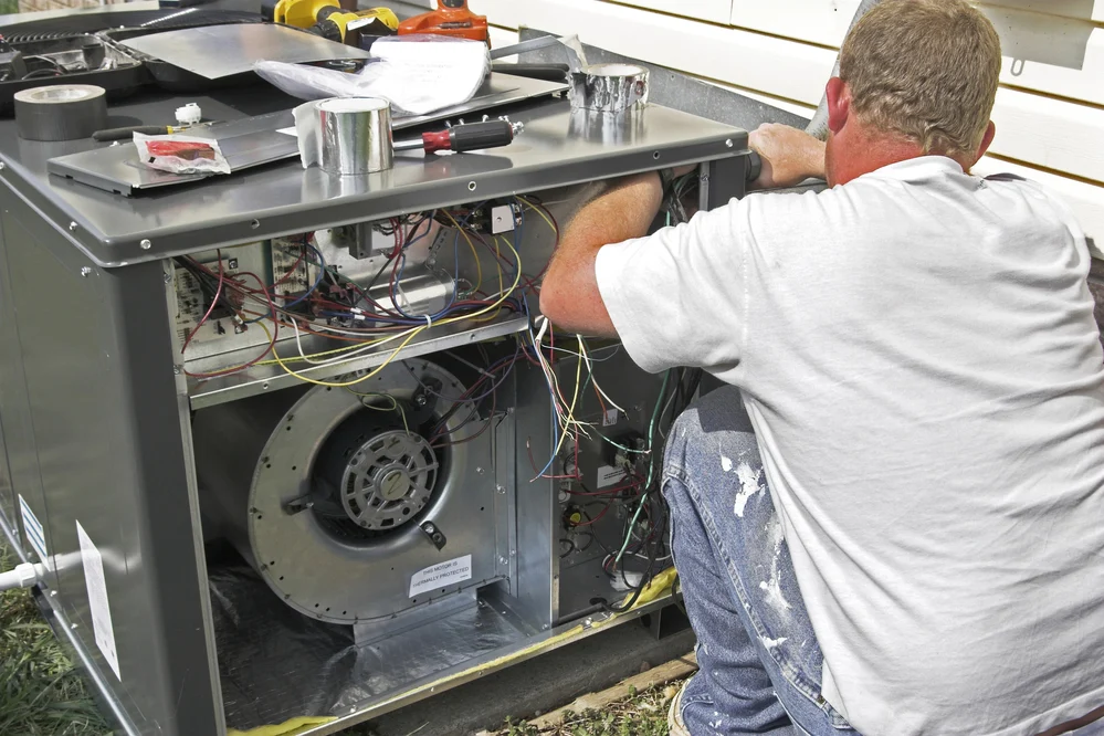 HVAC technician performing maintenance on a commercial air conditioning unit with exposed wiring and internal components.