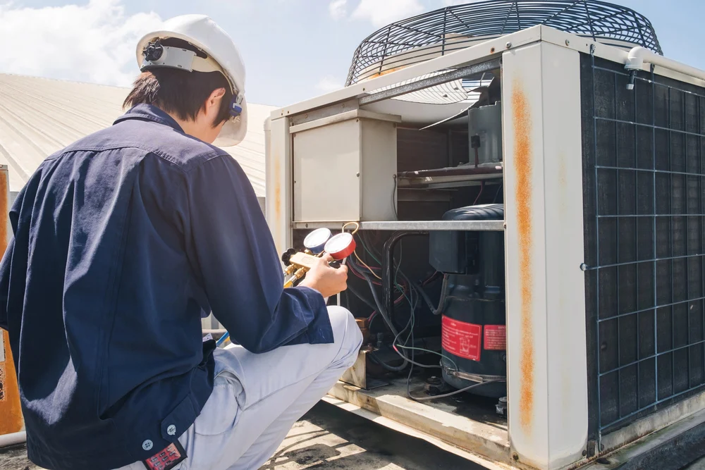 Technician performing maintenance on a commercial rooftop HVAC unit with pressure gauges.