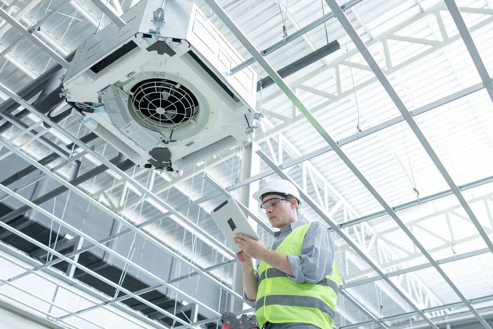 Inspector evaluating a commercial ceiling-mounted HVAC system for compliance and performance.