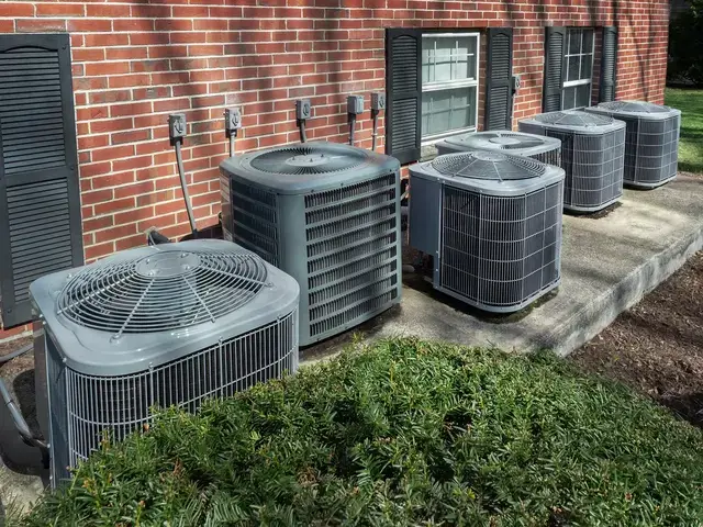 Multiple residential HVAC units outside a multi-family brick building.