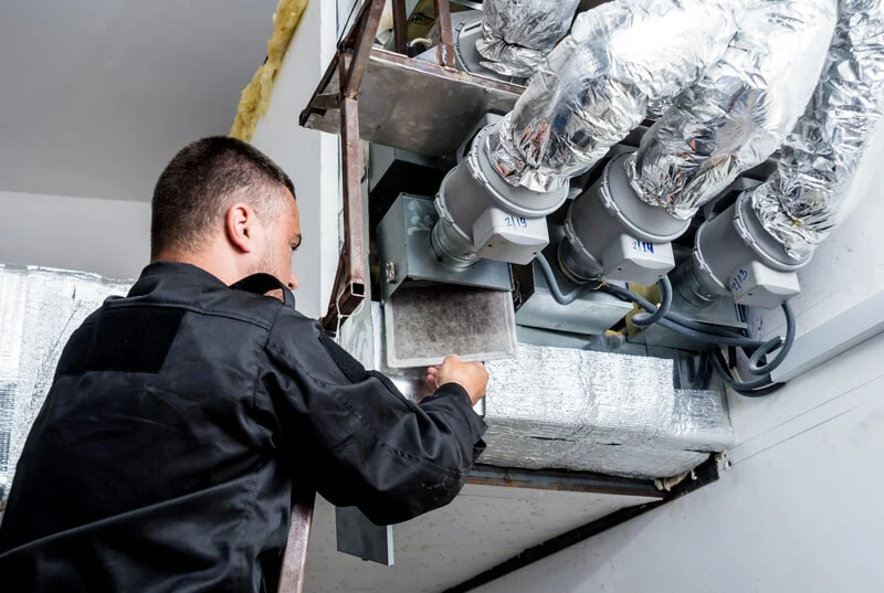Technician inspecting and cleaning ductwork in a commercial HVAC system.