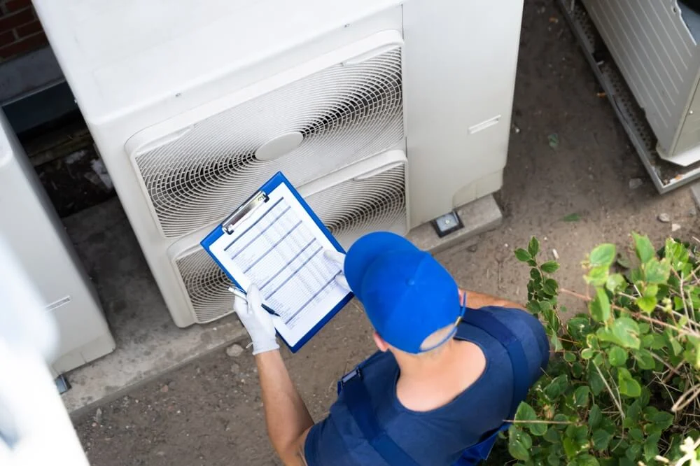 HVAC technician inspecting a commercial outdoor AC unit with a maintenance checklist on a clipboard.