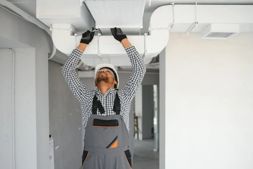 HVAC technician inspecting and cleaning commercial air ducts inside a building to improve airflow and indoor air quality.