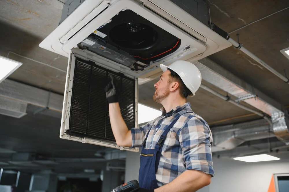 Technician performing commercial HVAC maintenance in a San Diego office building ceiling unit.